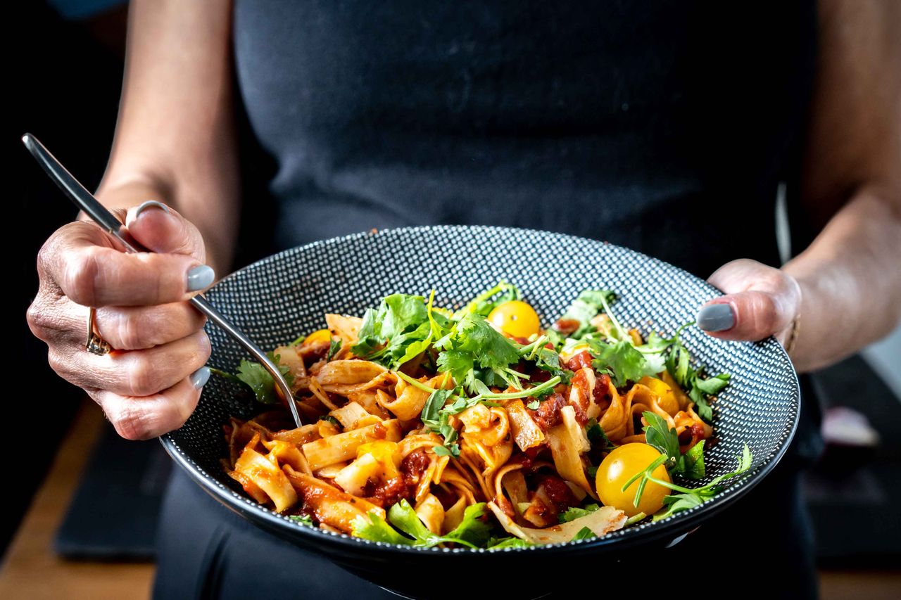 services-01 Close-up of woman holding a bowl of fresh pasta garnished with cilantro and cherry tomatoes.